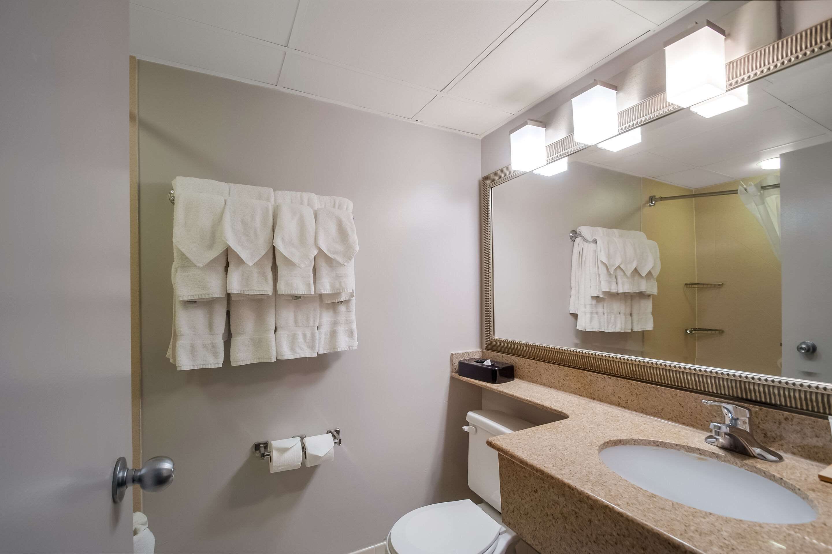 A bathroom with a toilet, sink, and a large mirror. There are multiple white towels hanging on the wall.