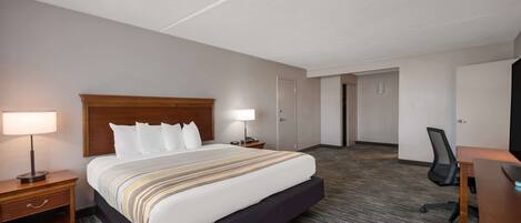 A hotel room with a large bed, a desk, a chair, a nightstand, and a lamp.