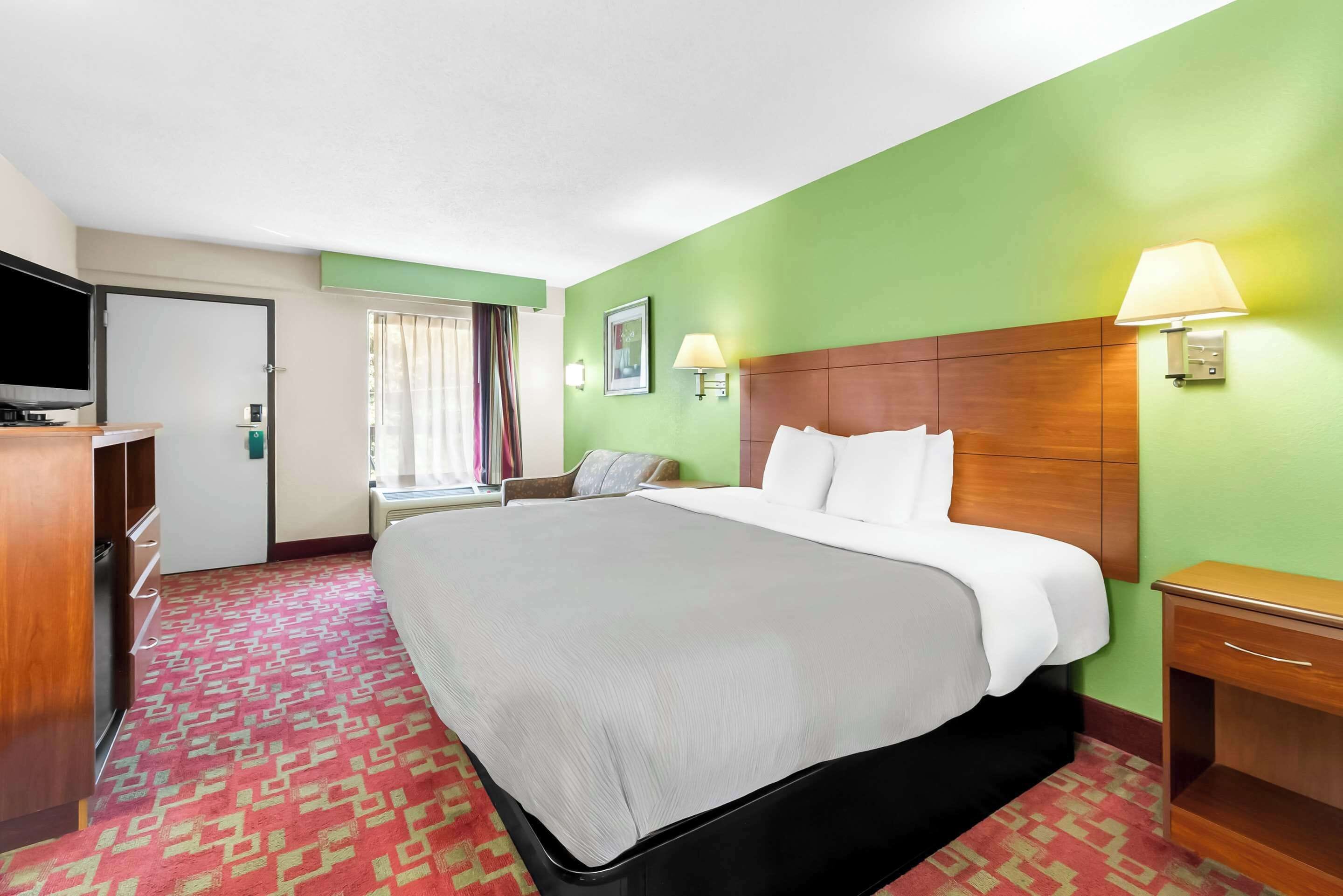 A hotel room with a large bed, a television, a desk, and a window with curtains.