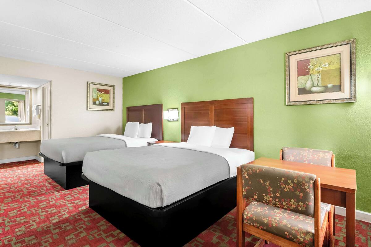 Een hotelkamer met twee bedden, een houten tafel, een bloemenstoel en een groene wand.