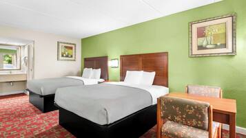 A hotel room with two beds, a wooden table, a floral chair, and a green wall.