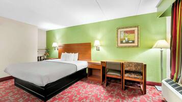A hotel room with a bed, desk, chair, and a painting on the wall.