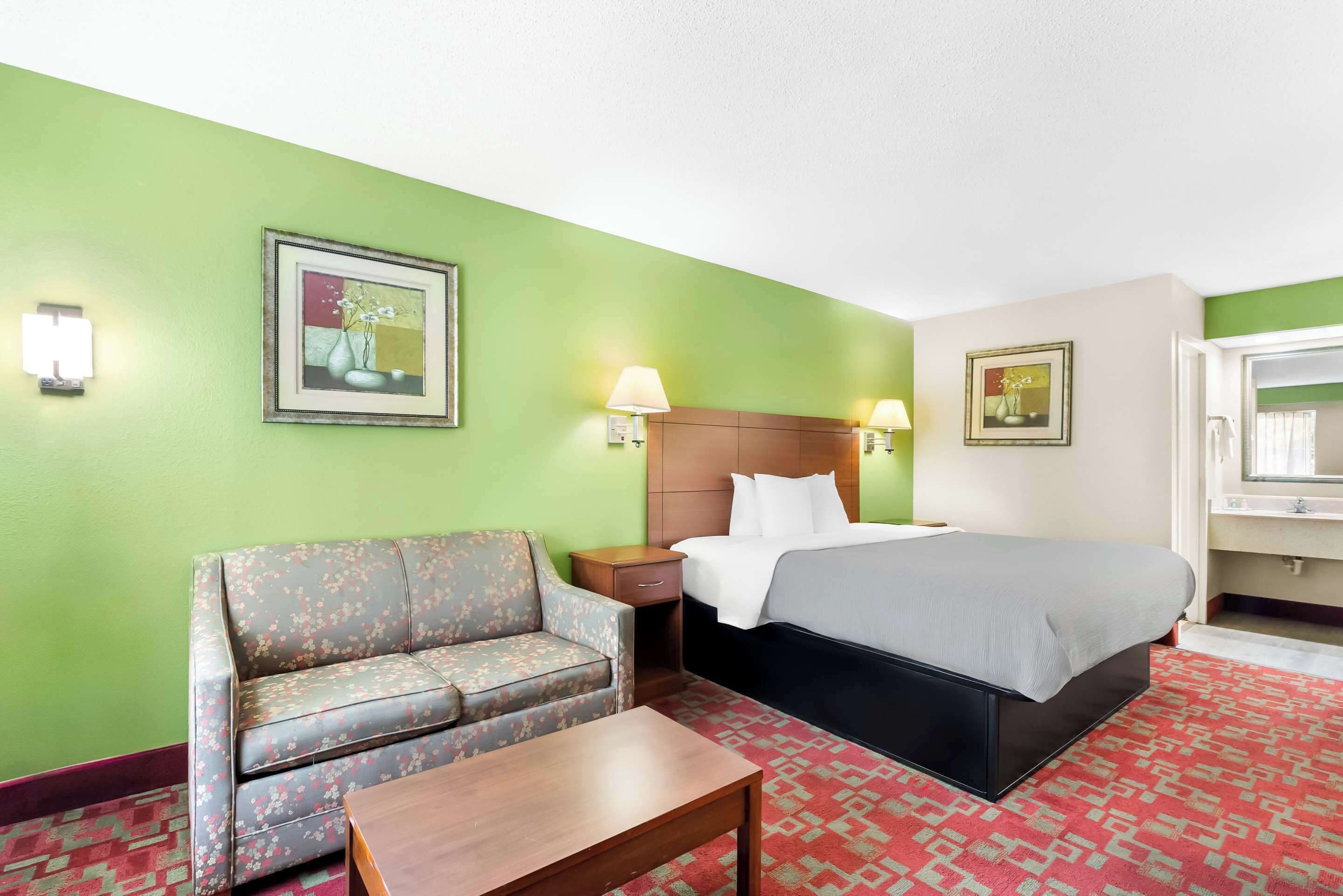 Una habitación de hotel con cama, sofá, mesita de noche y una mesa.