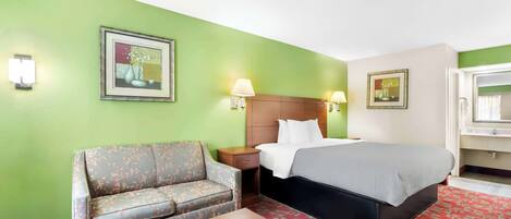Una habitación de hotel con cama, sofá, mesita de noche y una mesa.