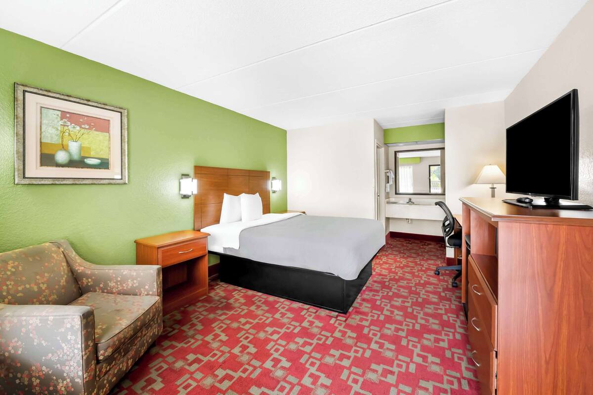 Een hotelkamer met een bed, een bureau, een televisie, een stoel en een schilderij aan de muur.