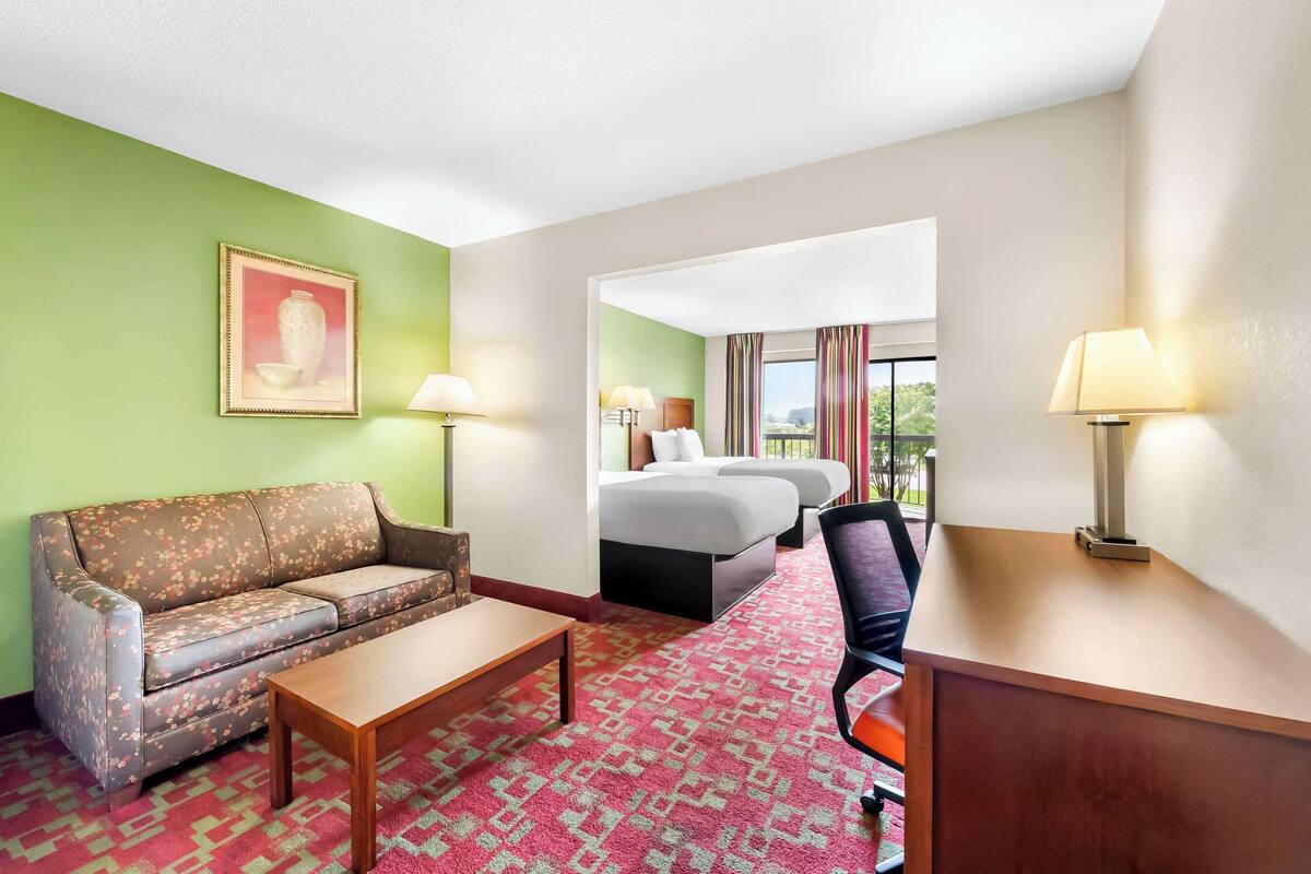 Een hotelkamer met een bank, een bureau, een stoel, een bed en een raam met gordijnen.