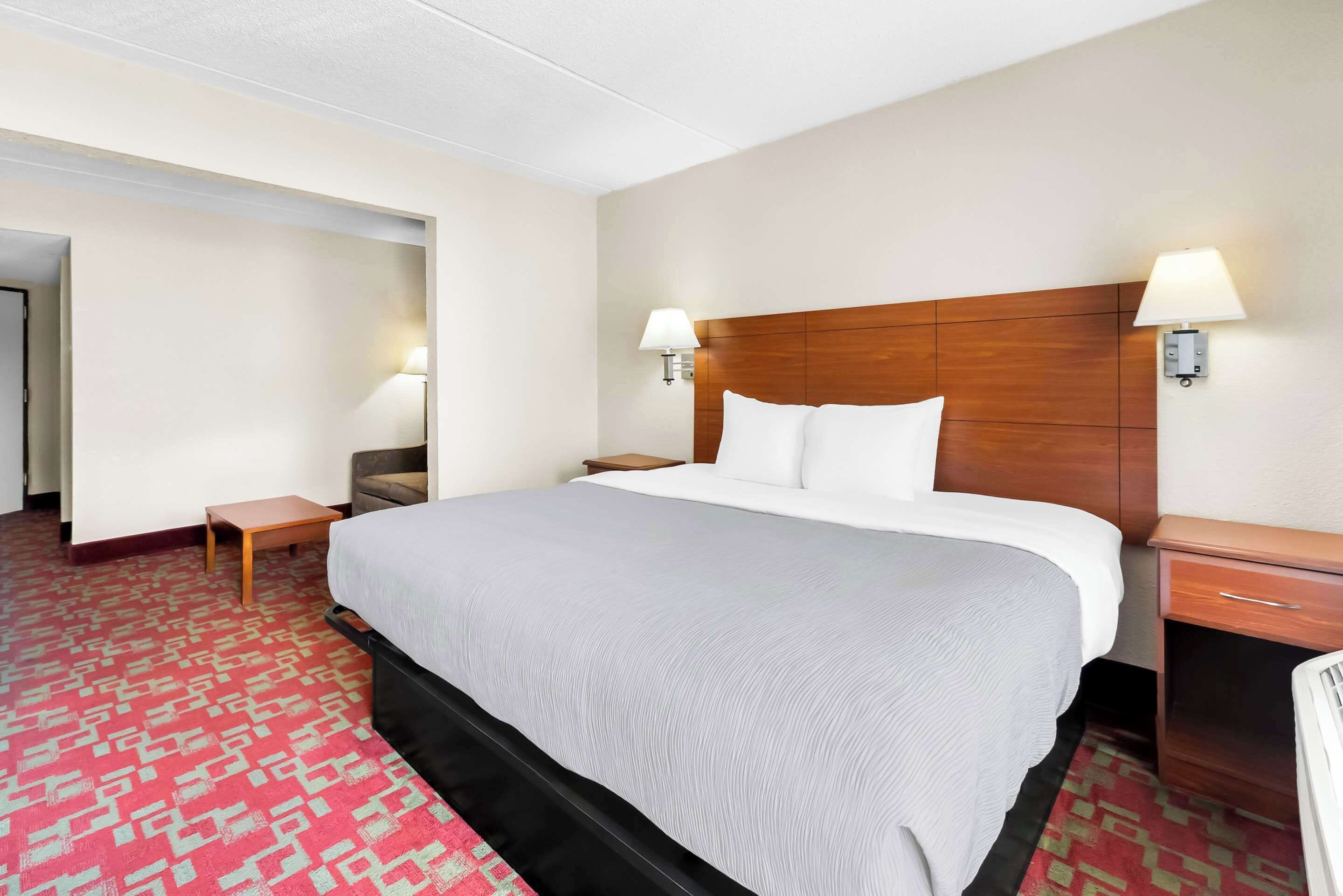 A hotel room with a large bed, two bedside tables, a nightstand, a wooden headboard, and two wall-mounted lamps.