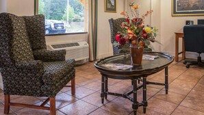 Un vestíbulo de hotel con dos sillones estampados, una mesa redonda con un florero y un reloj en la pared, además de un cuadro enmarcado.