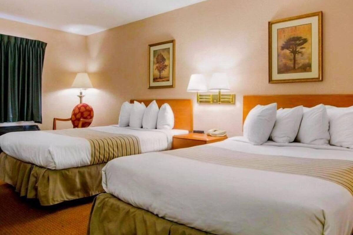 A hotel room with two beds, a desk, a chair, lamps, and artwork on the walls.