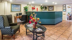 Un área de recepción con un mostrador verde, una computadora, cuadros enmarcados y un arreglo floral sobre una mesa.