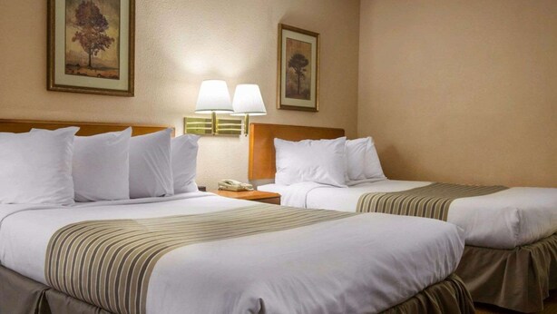 Habitación de hotel con dos camas, paredes color beige y cuadros enmarcados sobre las camas.