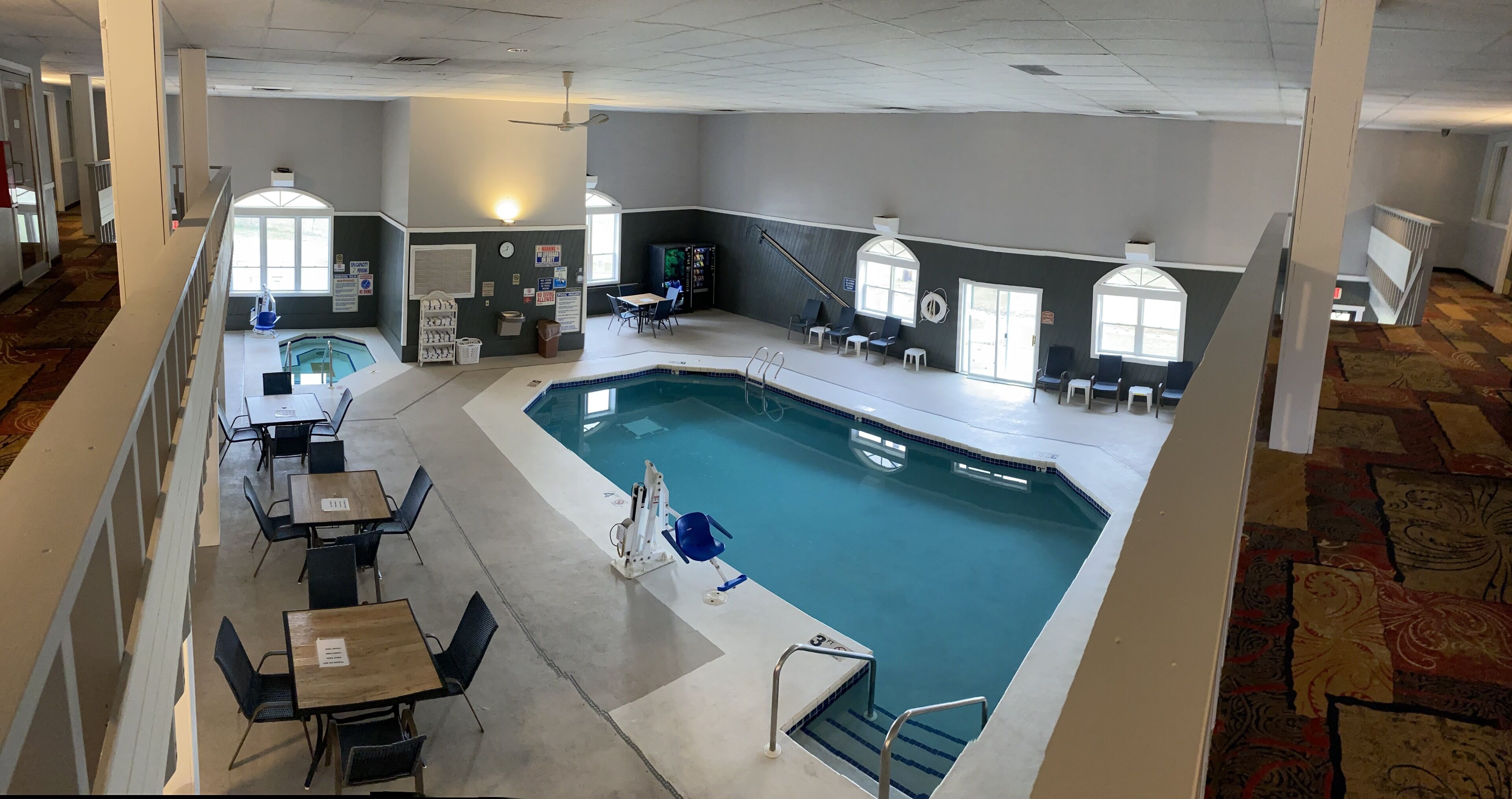 Un vestíbulo de hotel con una amplia piscina interior, zonas de estar y un mostrador de recepción.