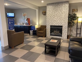 A hotel lobby with a checkered floor, a fireplace, sofas, a coffee table, and a reception desk with a computer monitor.