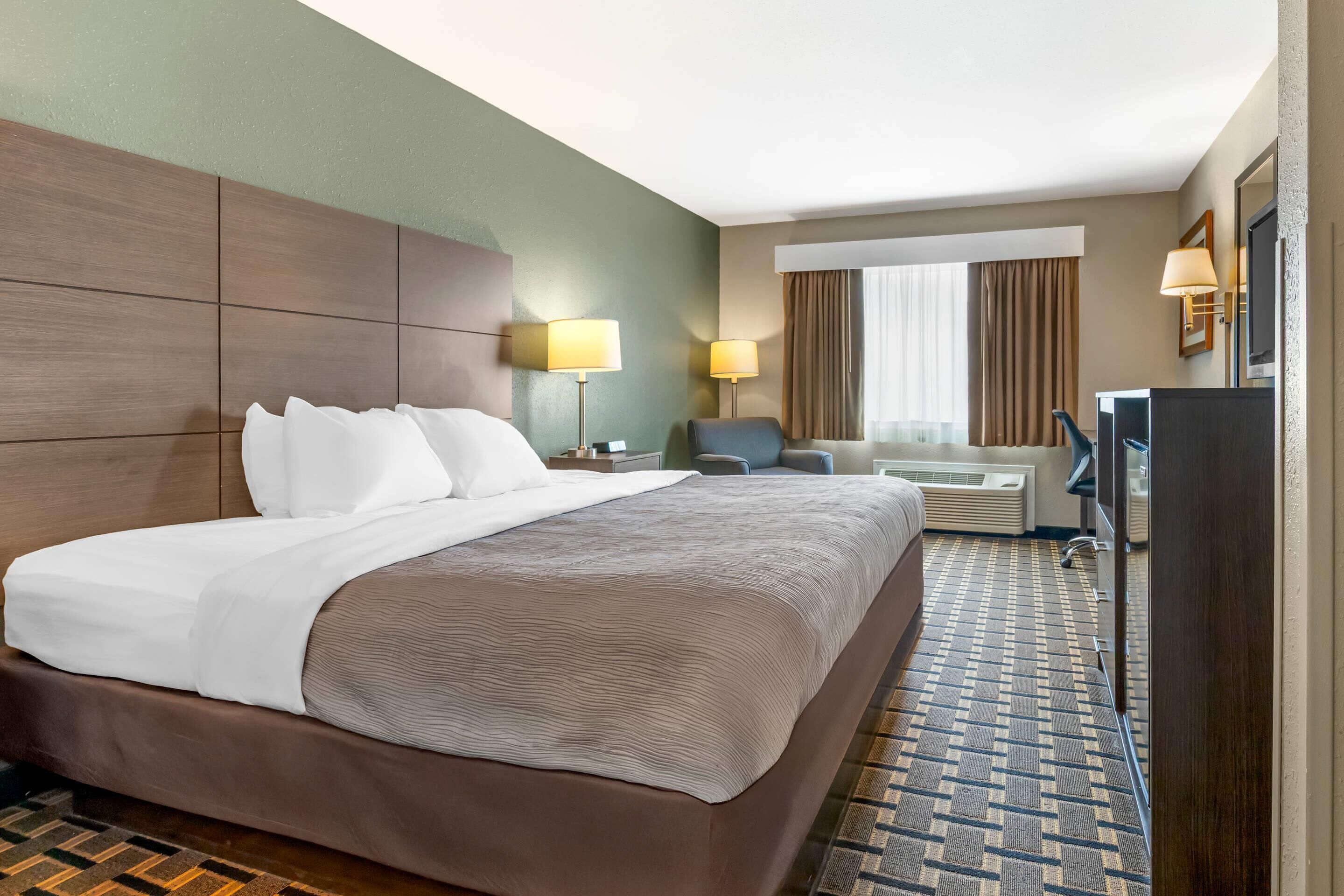 Habitación de hotel con una cama grande, dos lámparas de noche, un escritorio con una silla, un televisor y una ventana con cortinas.