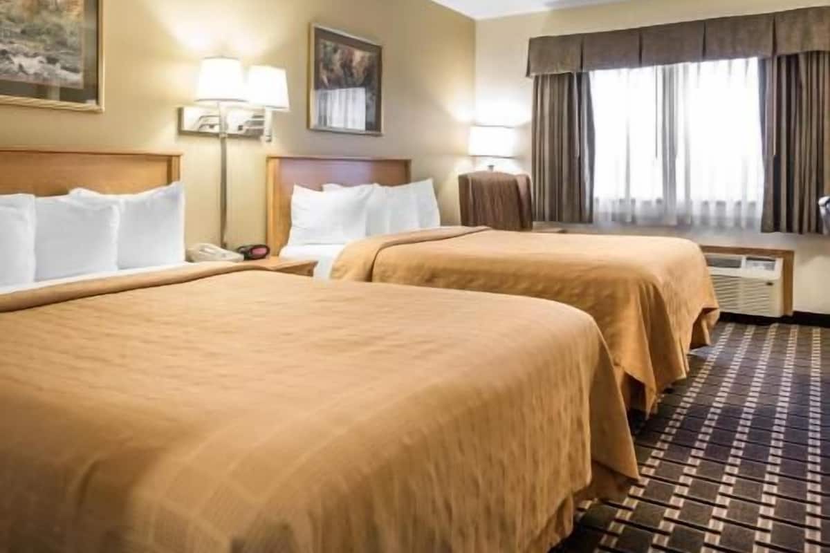A hotel room with two beds, a desk, a chair, a lamp, and a painting on the wall.