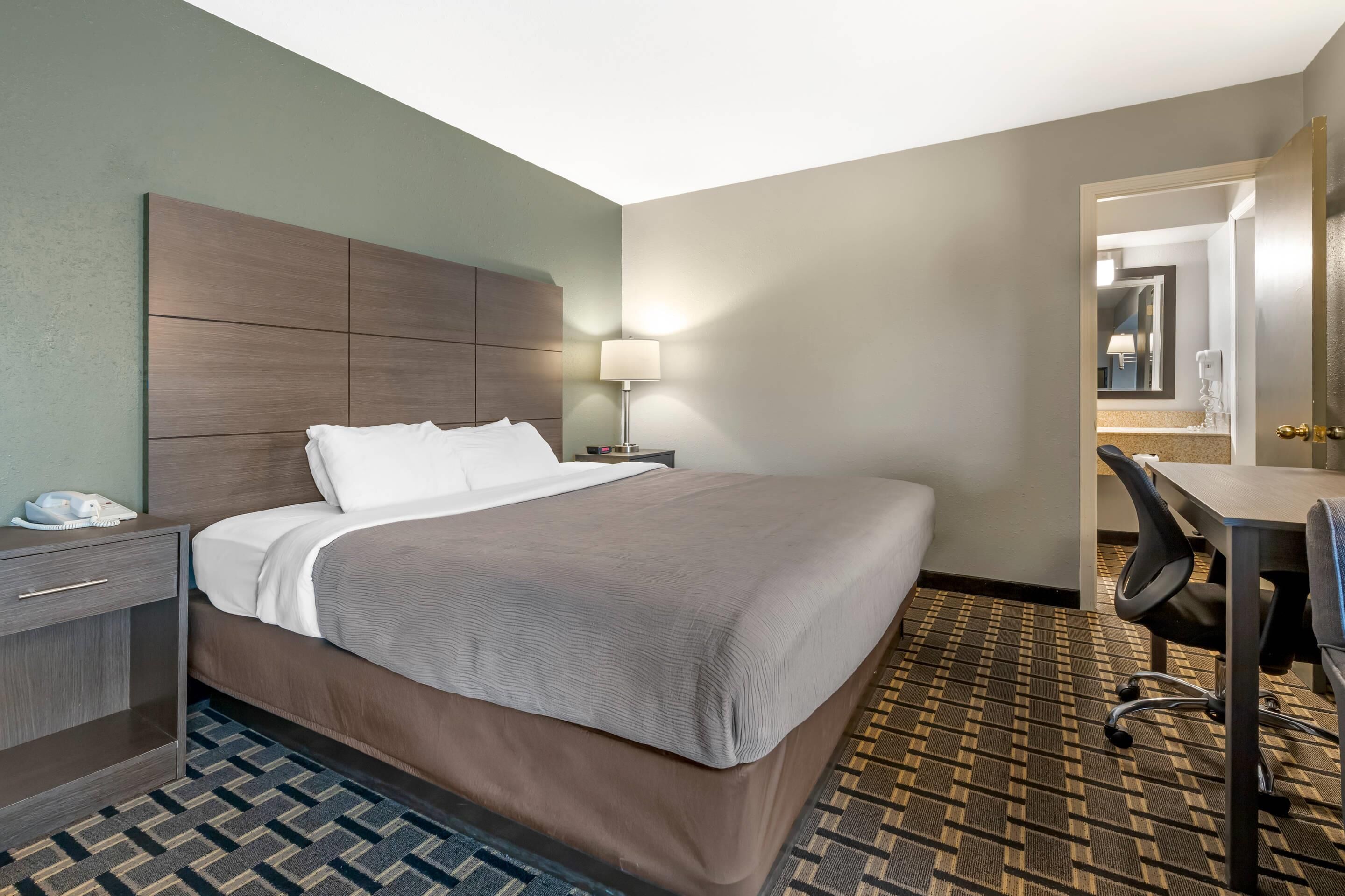 Una habitación de hotel con una cama grande, un escritorio, una silla, una mesita de noche y una lámpara.