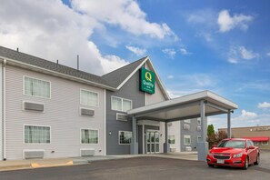 Un hôtel de la chaîne Quality Inn doté d’une entrée couverte et devant lequel est garée une voiture rouge.