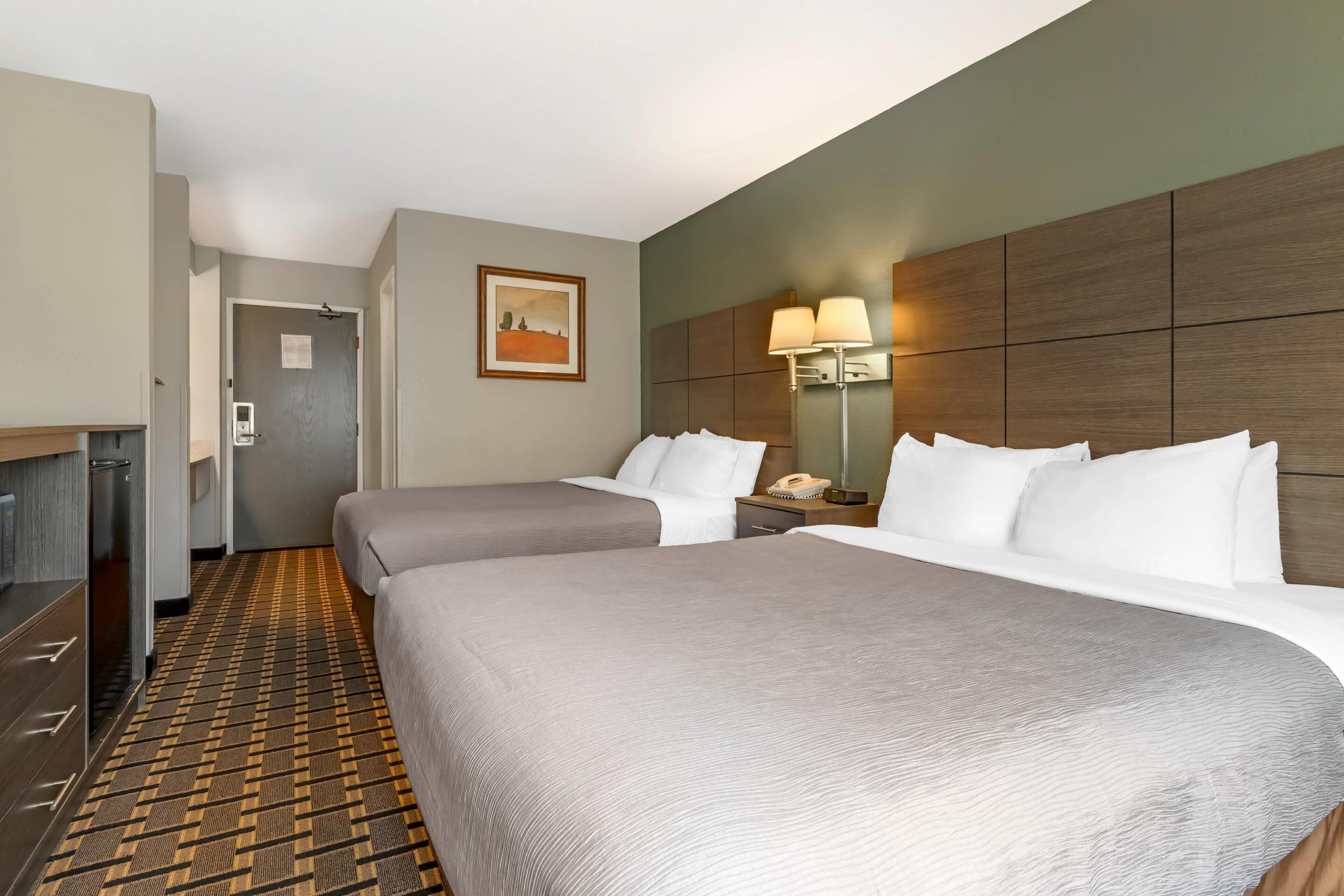 Een hotelkamer met twee bedden, een bureau, een lamp en een schilderij aan de muur.