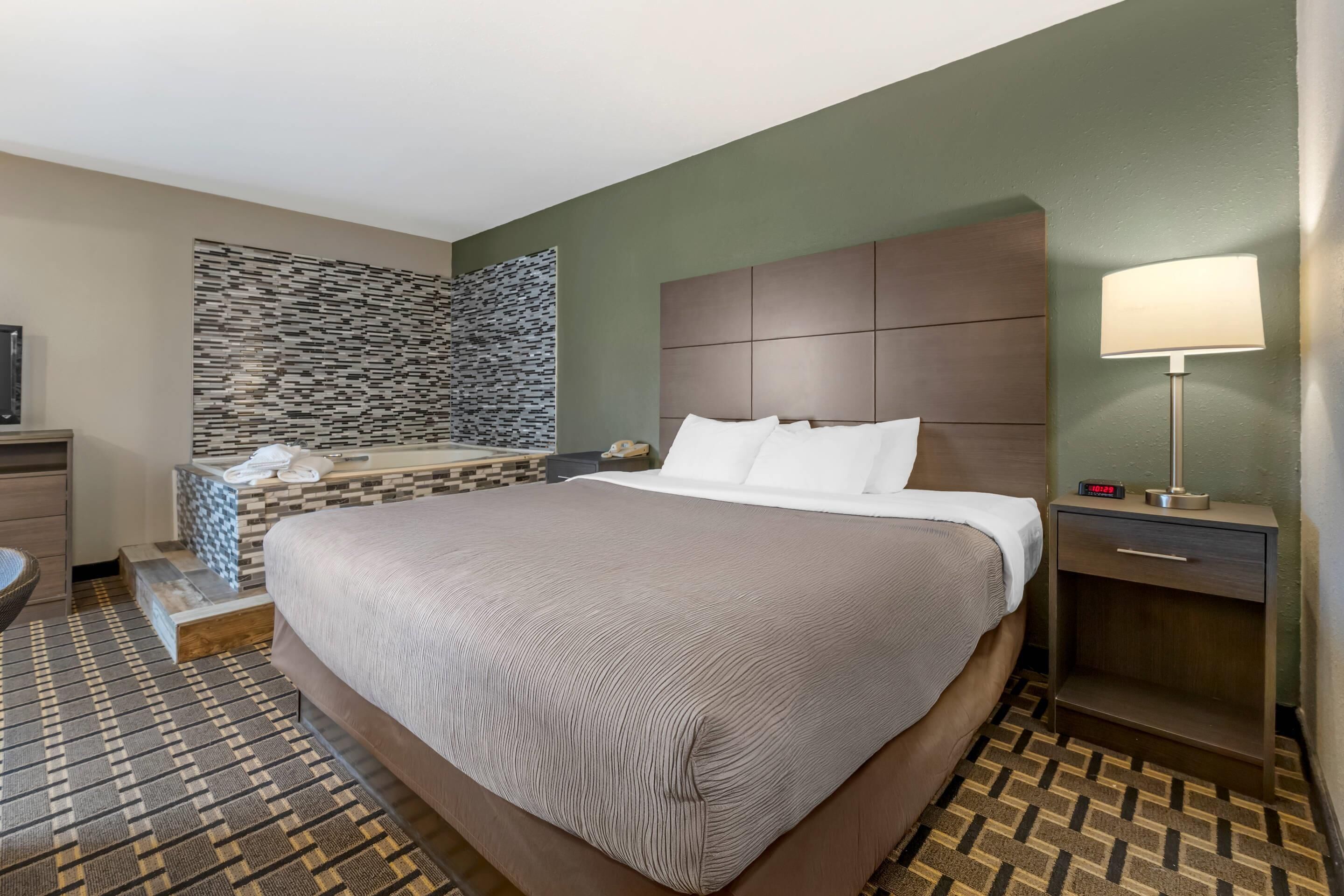 Una habitación de hotel con una cama grande, un baño pequeño, una pared de piedra y una mesita de noche con una lámpara.