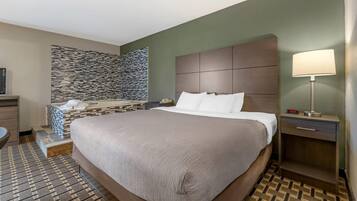 Una habitación de hotel con una cama grande, un baño pequeño, una pared de piedra y una mesita de noche con una lámpara.