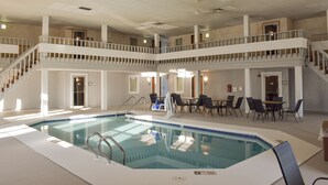 An indoor swimming pool with a multi-level balcony, seating area, and a staircase.