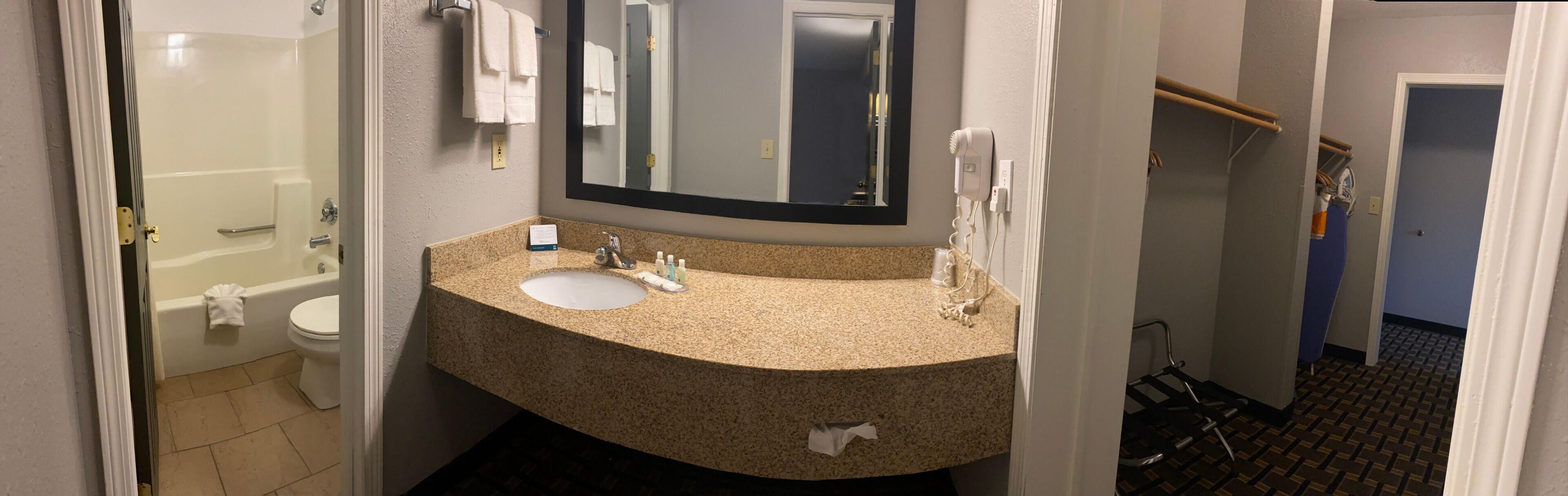 A bathroom with a sink, mirror, and towel rack. There is a shower area visible in the background.