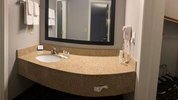 A bathroom with a sink, mirror, and towel rack. There is a shower area visible in the background.