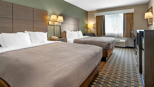 A hotel room with two beds, a desk, a chair, a TV, and a window with curtains.