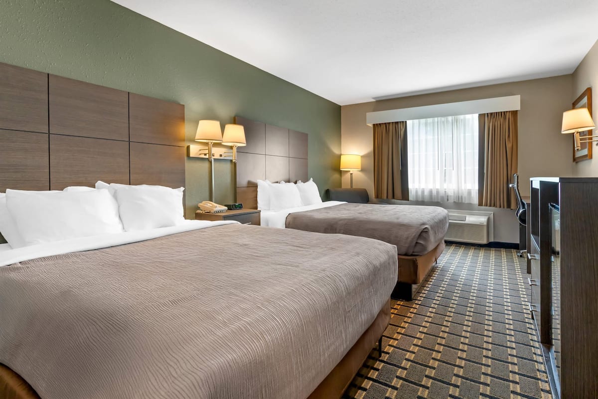 A hotel room with two beds, a desk, a chair, a TV, and a window with curtains.