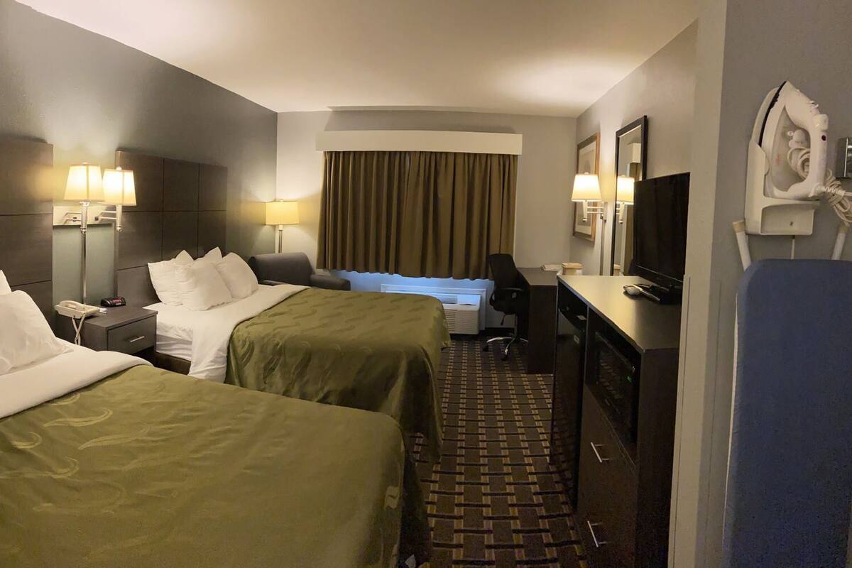 A hotel room with two beds, a desk, a television, a mirror, and a wall-mounted iron.