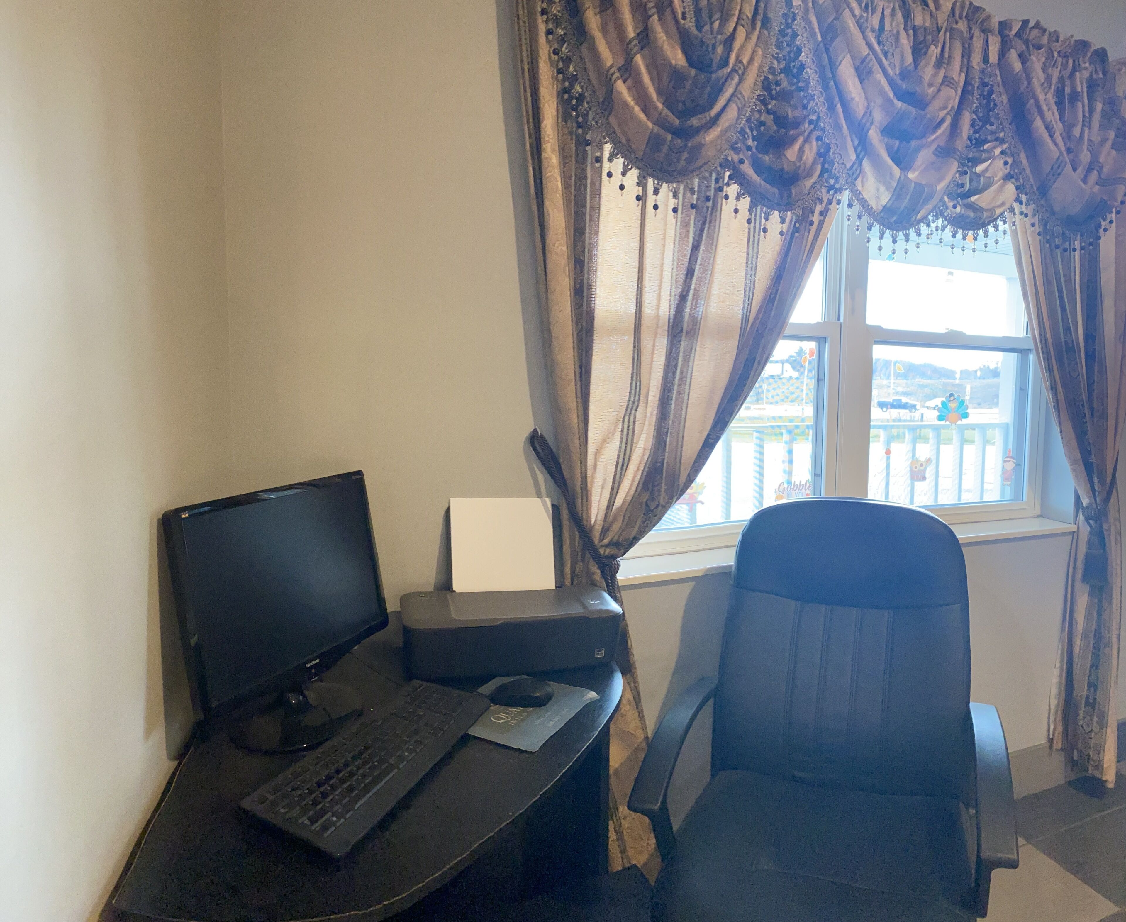 A workspace with a computer, keyboard, mouse, and printer on a desk, a chair, and a window with curtains.