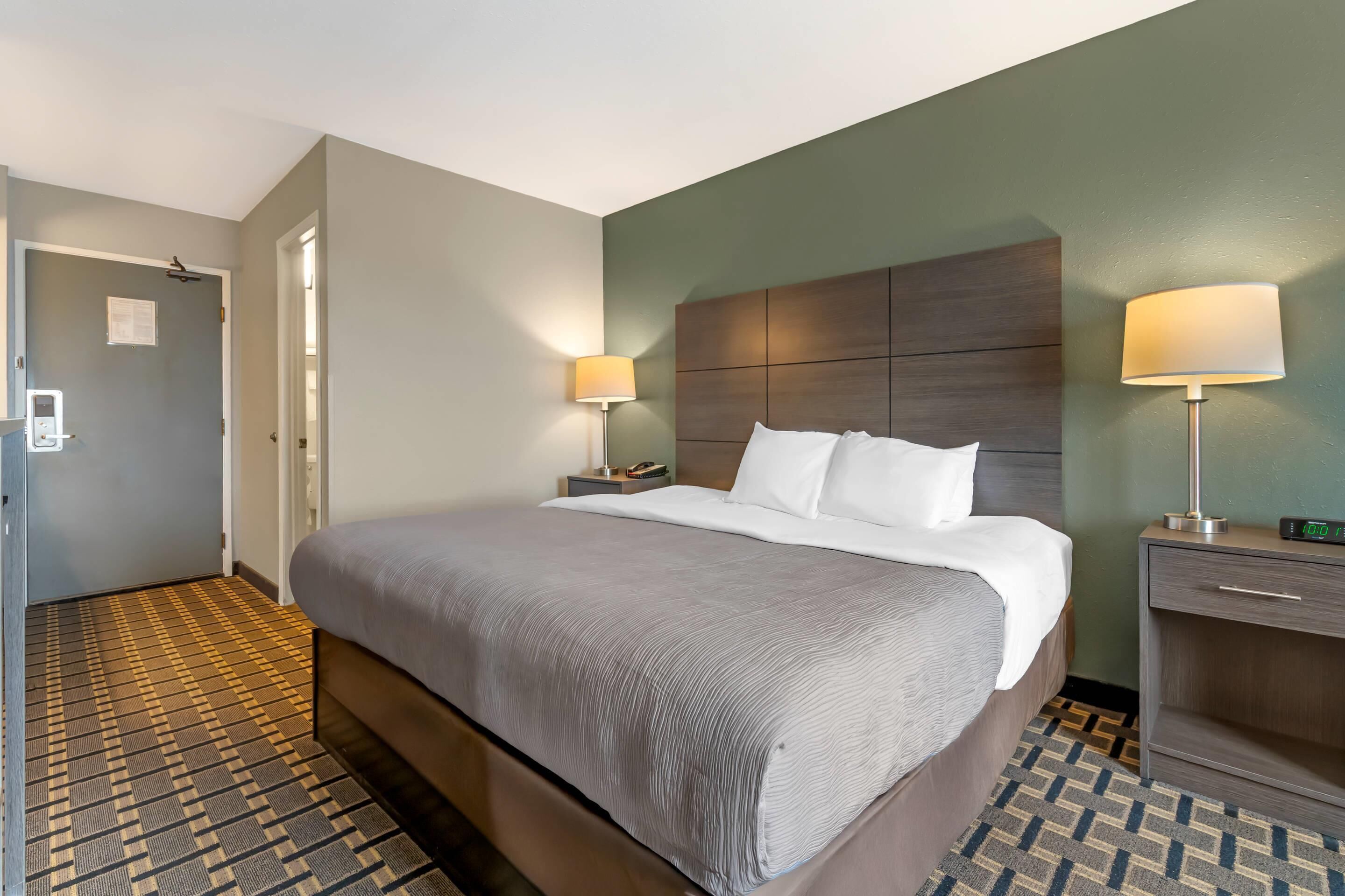 Une chambre d’hôtel avec un grand lit, deux tables de chevet avec des lampes, une tête de lit en bois et un sol à motifs.