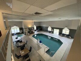 A large indoor swimming pool with a sunlit area and seating around it.