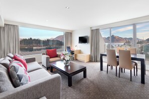 A modern hotel room with a large window offering a mountain view, a sofa, a dining table with chairs, and a flat-screen TV mounted on the wall. - Crowne Plaza Hotel Queenstown by IHG (Queenstown)