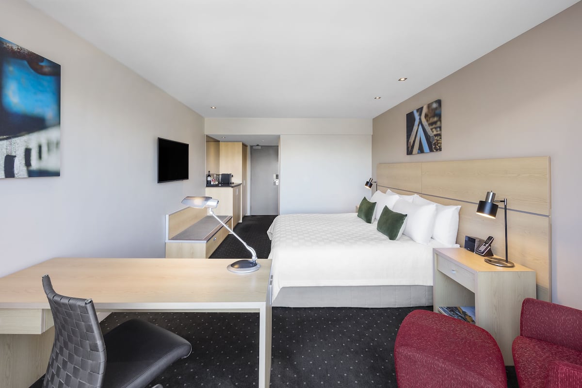 Een hotelkamer met een bed, bureau, stoel en een klein tafeltje met een lamp.