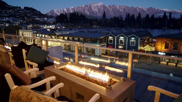 Een balkon met een vuurplaats, zitplaatsen en een uitzicht op besneeuwde bergen.