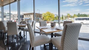 Un restaurant doté de grandes fenêtres, de chaises à motifs et offrant une vue sur la rue et les montagnes.