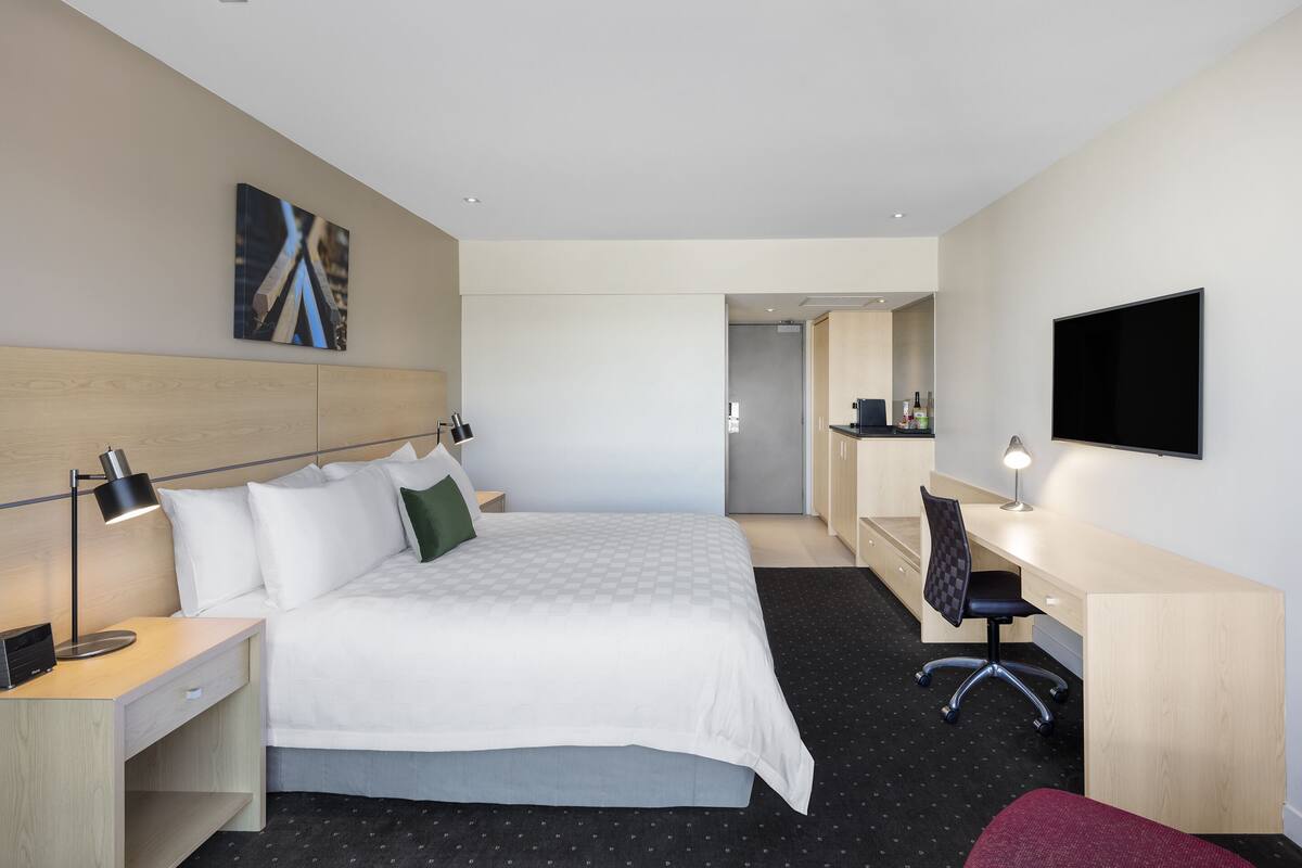 Hotelkamer met een bed, bureau, stoel, televisie en kunst aan de muur.
