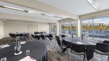 Un salón de conferencias con mesas redondas, sillas y vistas a montañas a través de amplias ventanas.