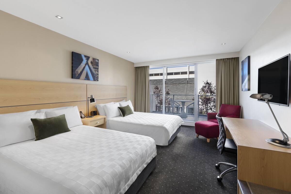 Een hotelkamer met twee bedden, een bureau, een stoel, een televisie en een raam met uitzicht.