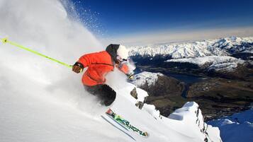 Eine Person fährt auf Skiern einen verschneiten Hang hinab, im Hintergrund sind schneebedeckte Berge zu sehen.