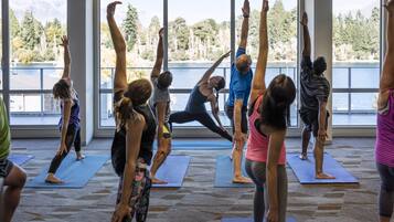 A group of people practicing yoga in a room with large windows overlooking a body of water and trees.