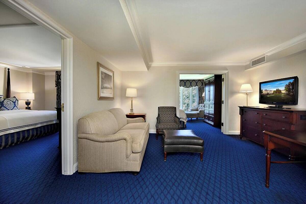 A hotel room with a bed, a sofa, a chair, a TV, and a dresser.