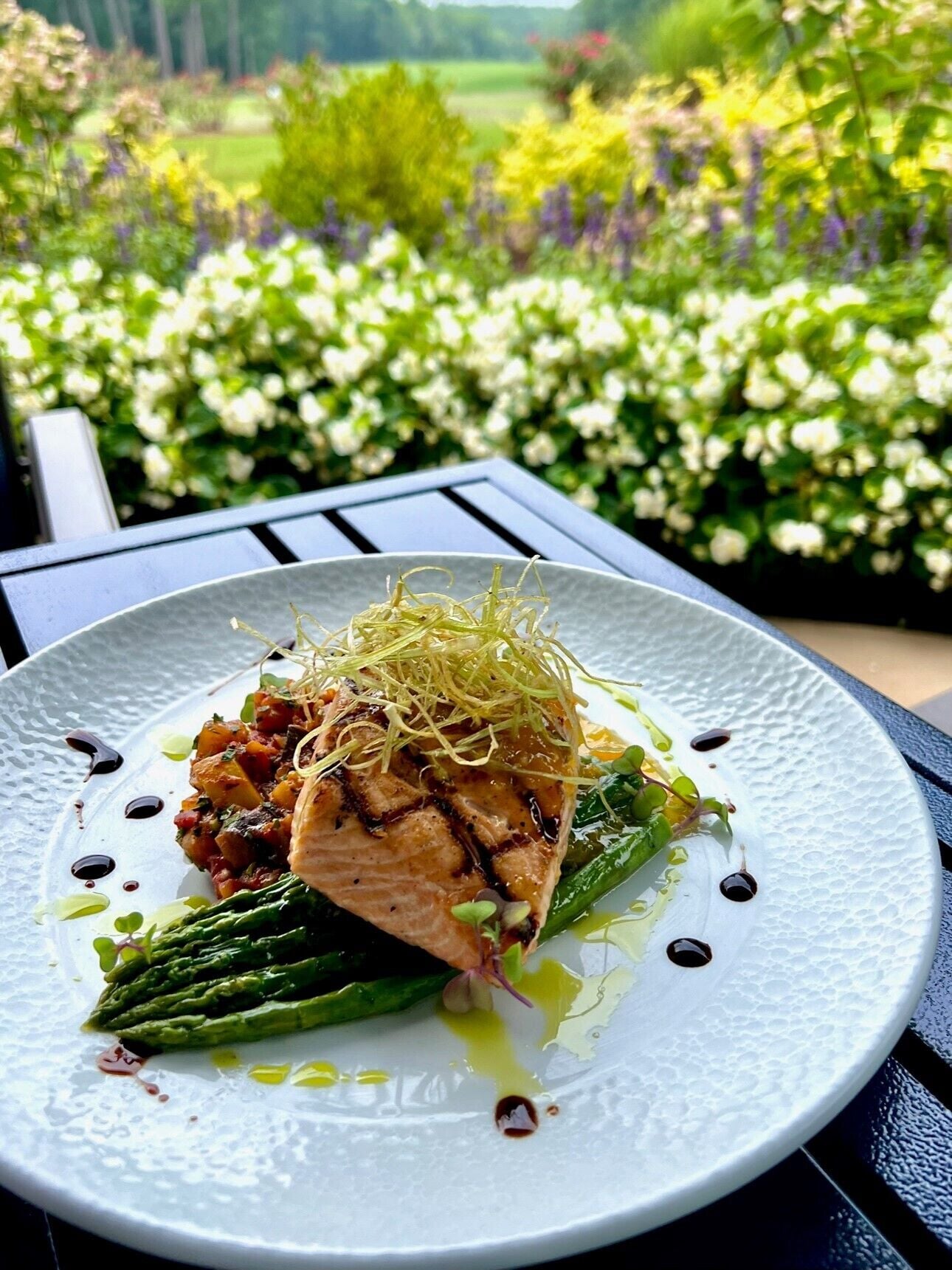 A plate of food with grilled salmon, asparagus, and a garnish on a white plate.