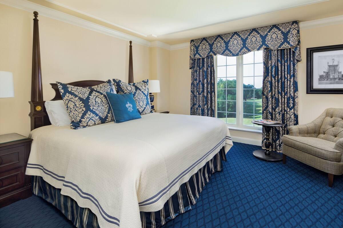 A four-poster bed with a white and blue bedspread, a blue and white patterned pillow, and a matching blue and white curtain.