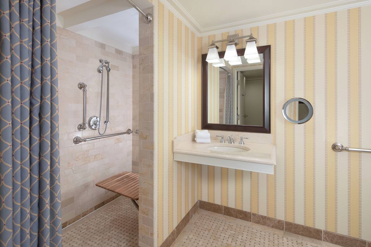A bathroom with a shower, a sink, a mirror, and striped wallpaper.