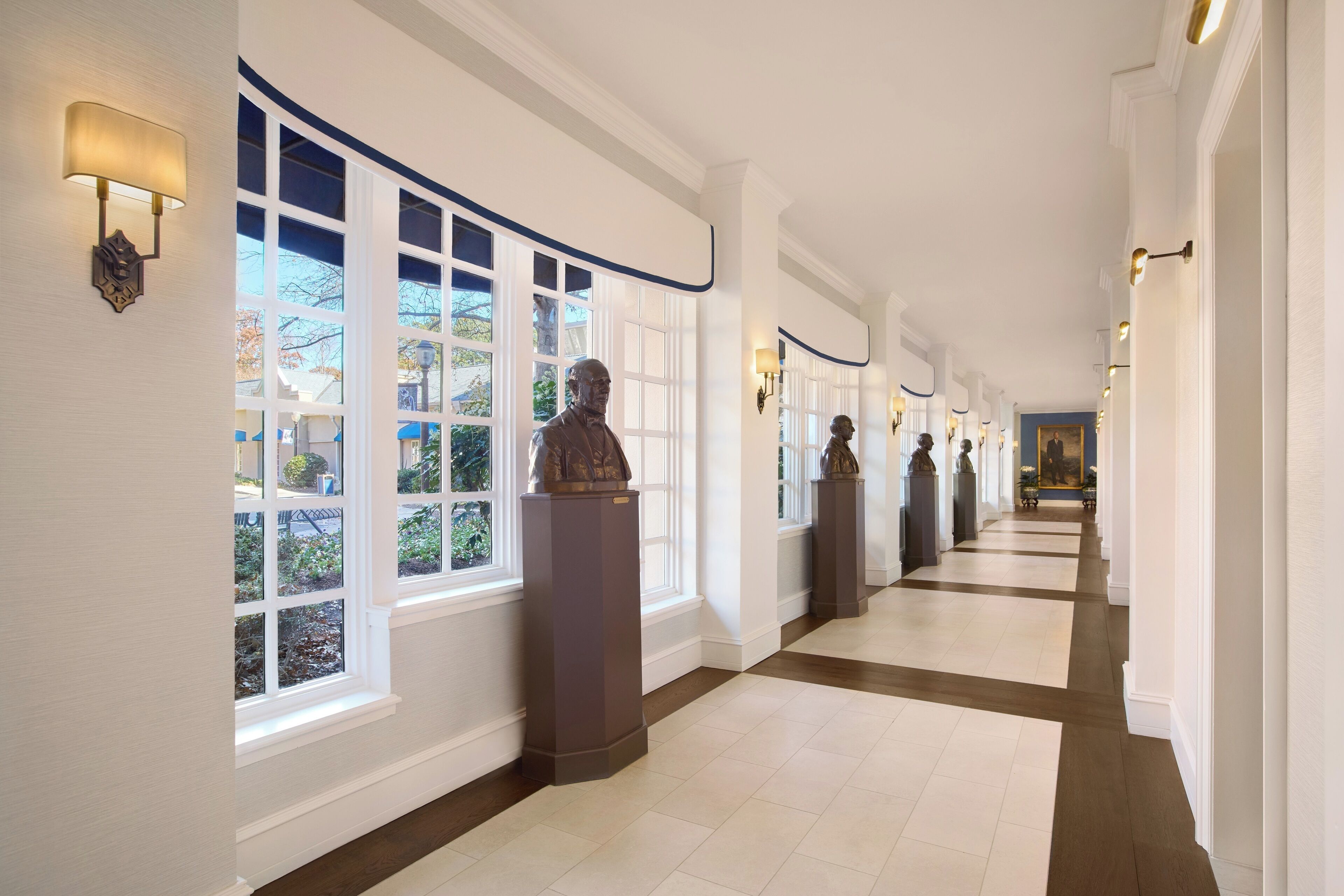 A long, well-lit hallway with large windows and statues along the walls.