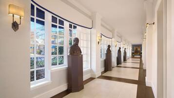 A long, well-lit hallway with large windows and statues along the walls.