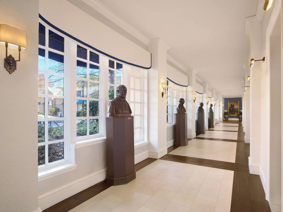 A long, well-lit hallway with large windows and statues along the walls.
