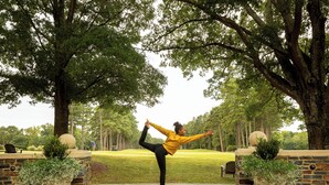 A person performing a yoga pose outdoors with trees and a golf course in the background.